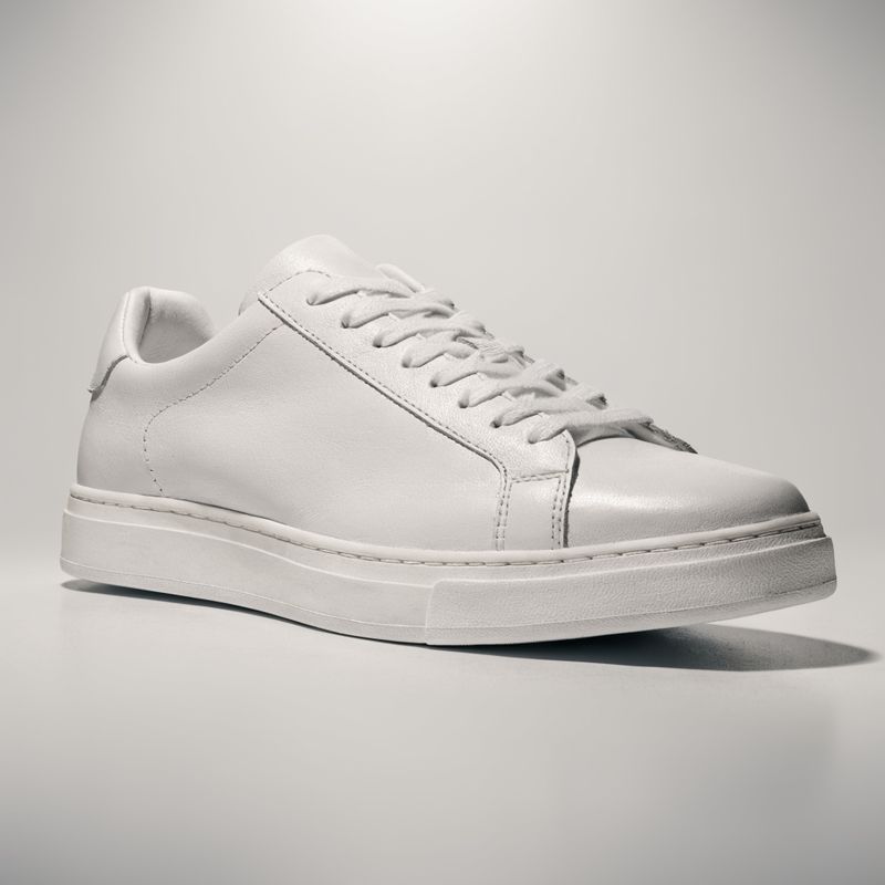 A pristine white leather sneaker with no branding on a pale grey seamless studio backdrop