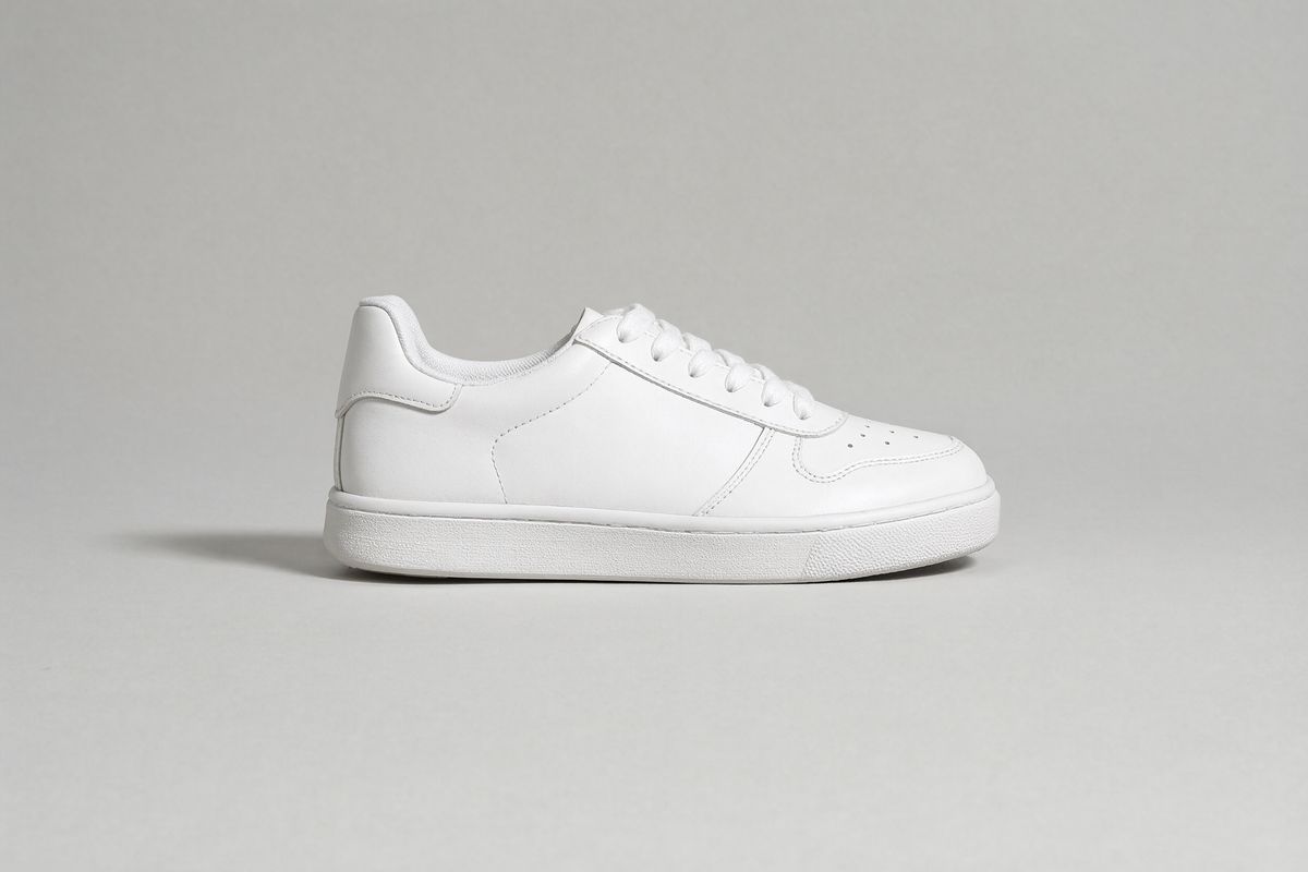 A white leather low-top sneaker in side profile with a perforated toe and a white cupsole on a light gray backdrop