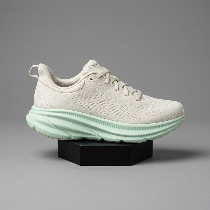 A packshot of an off-white mesh running shoe with a pale mint midsole on a low matte black stand against a seamless grey backdrop