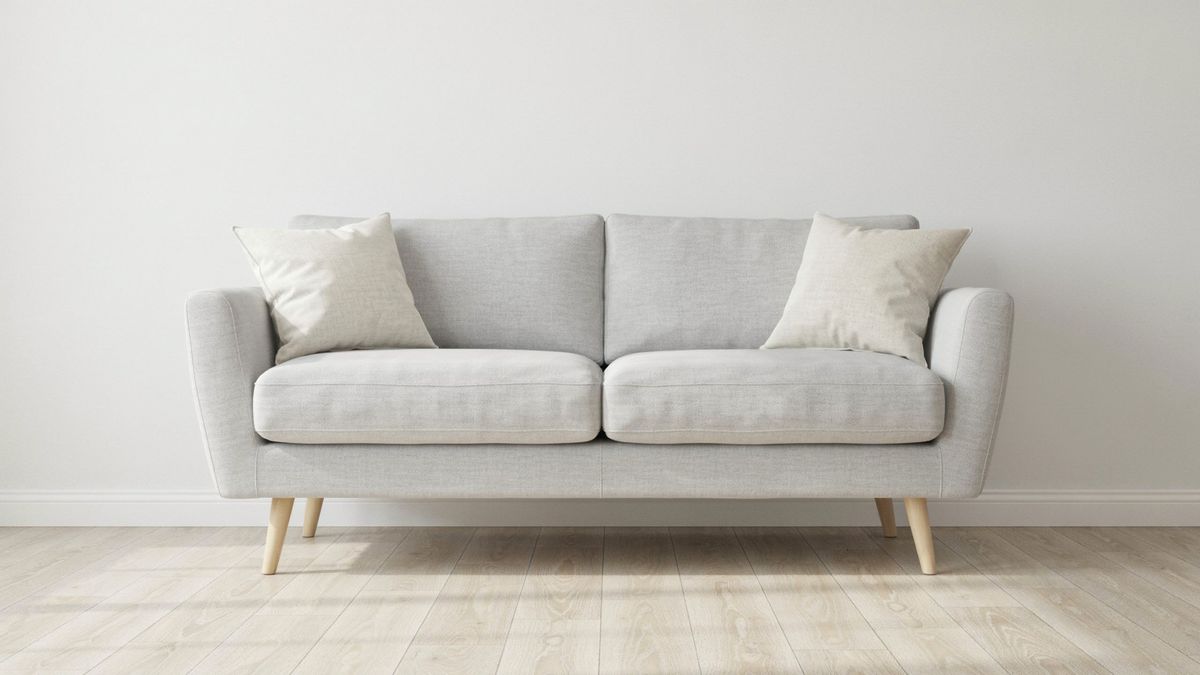 A light gray three-seat sofa against a white wall with two identical cream pillows, one in each corner