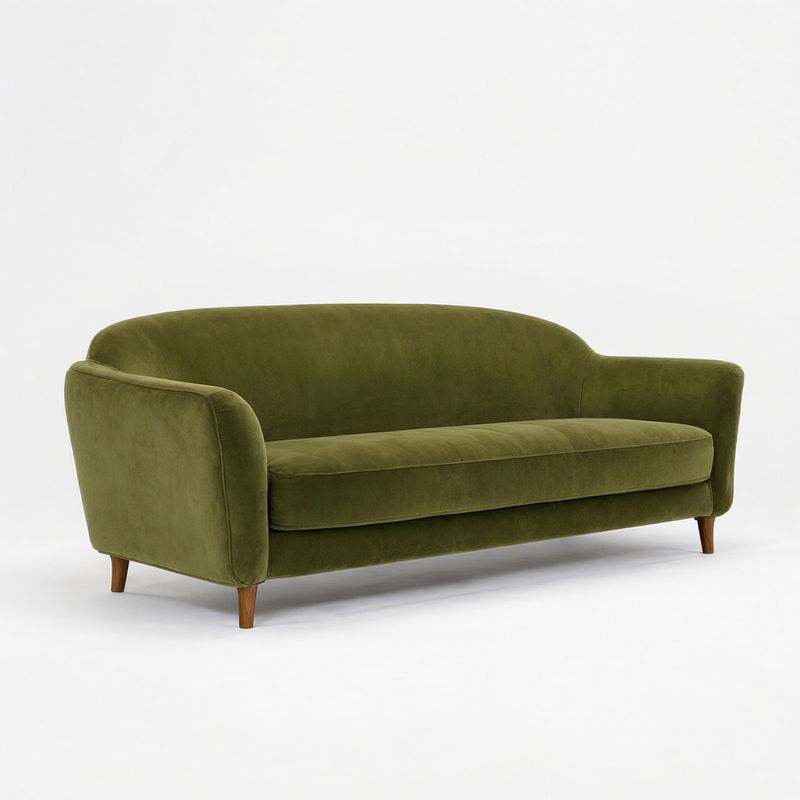 A low olive green velvet three-seat sofa with rounded arms and walnut legs on white