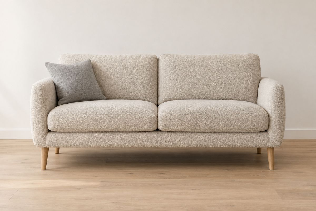 A two-seater sofa upholstered in oatmeal bouclé with pale oak legs and a single grey cushion, staged against a warm white wall on a light oak floor