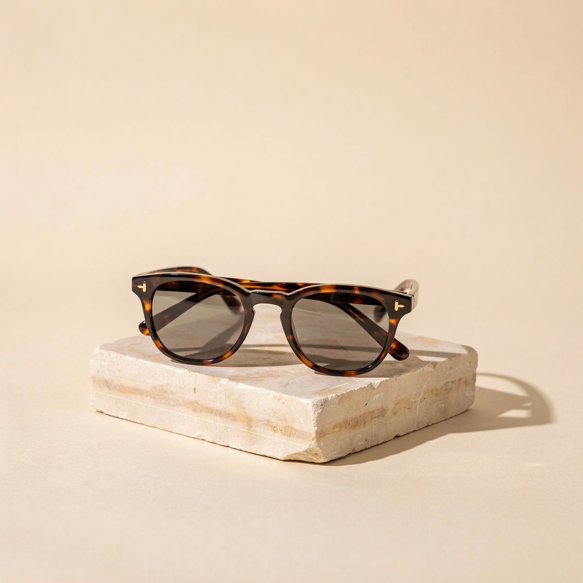 Tortoiseshell sunglasses on a pale sandstone block against a warm beige background, with a crisp shadow to the right