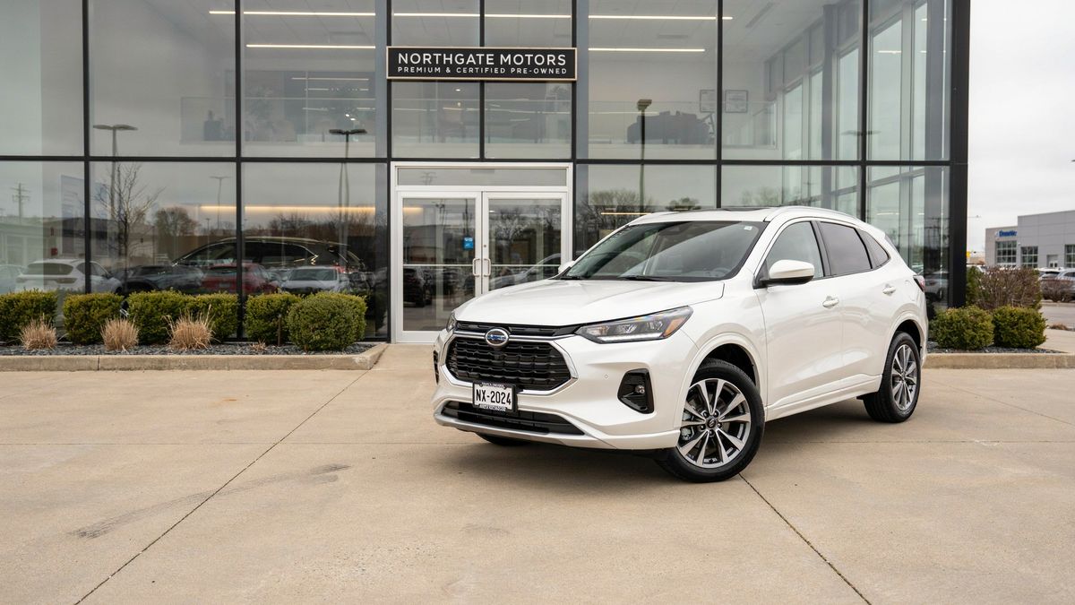 A white compact SUV at a three-quarter angle on a concrete forecourt in front of a glass showroom