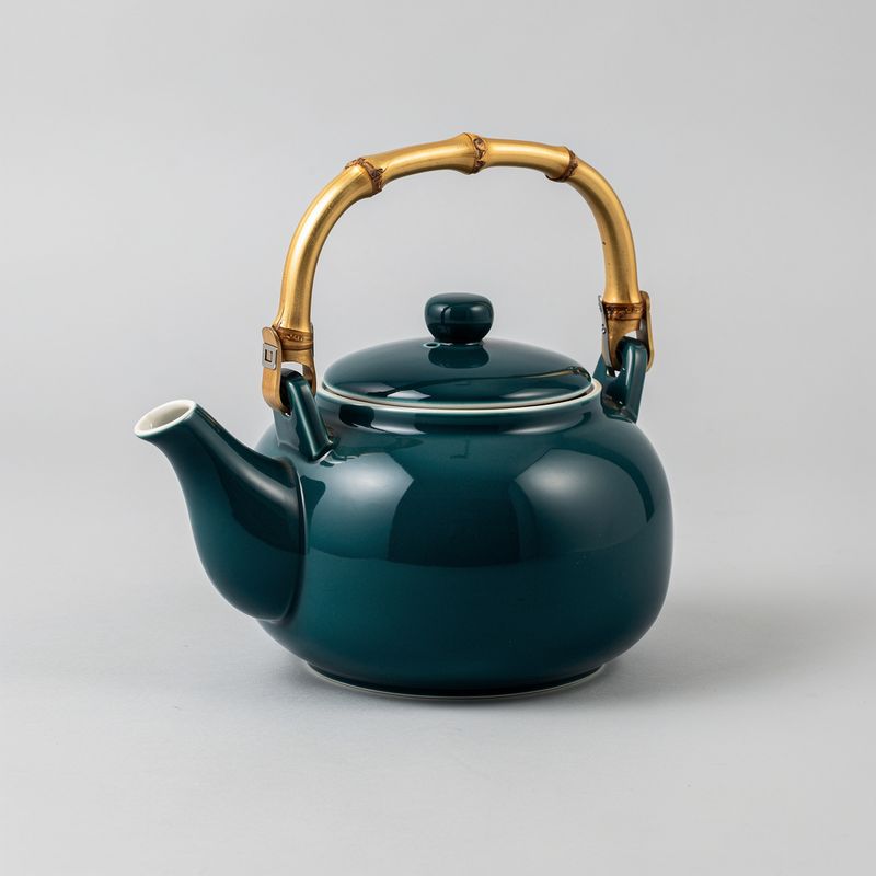 A glossy deep-teal ceramic teapot with a curved spout and a bamboo handle, centered on a plain gray background