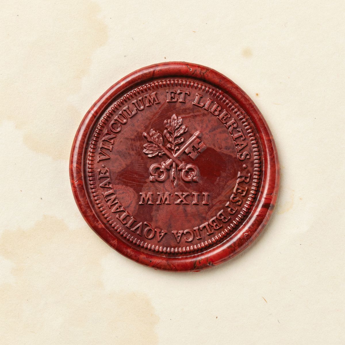 A crimson wax seal on cream parchment, with 'VINCULUM ET LIBERTAS' arcing along the top rim upright and 'RESPVBLICA AQVITANIAE' arcing along the bottom rim with the letters rotated to follow the curve, surrounding an embossed oak-branch-and-key emblem and the Roman numerals 'MMXII'