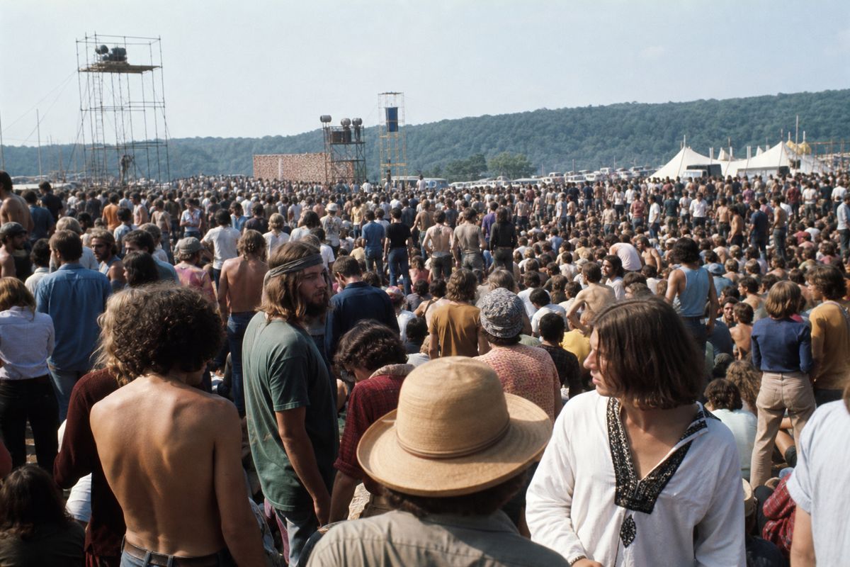 A large outdoor crowd scene in Bethel, New York on August 16, 1969, with period-accurate clothing and staging